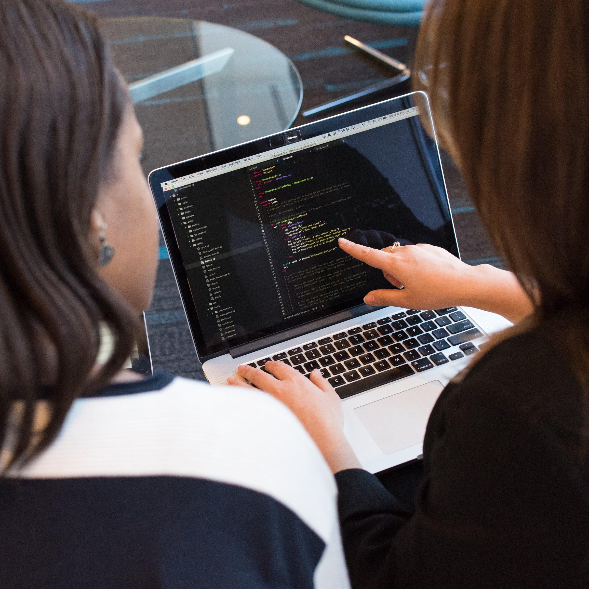 Two people review website code on a laptop, with one pointing to the screen.