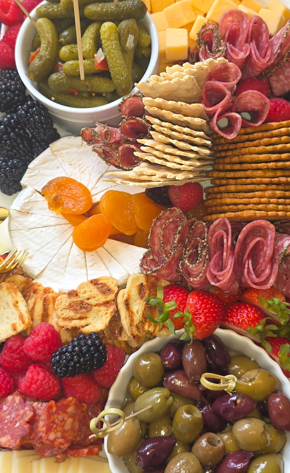 A colorful platter of cheeses, meats, crackers, fruit, and pickles.